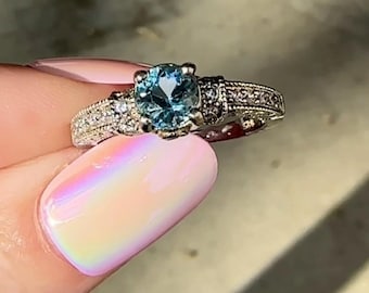 May include: A silver ring with a blue gemstone surrounded by smaller clear gemstones.