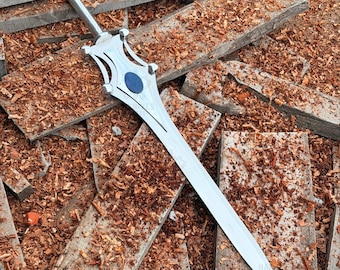 Op de afbeelding: Een zilverkleurig metalen zwaard met een puntig blad, een pareerstang met symmetrische gebogen uitsparingen en een centrale ovaalvormige blauwe inleg. Het handvat is cilindervormig met een afgeronde pommel aan het uiteinde.