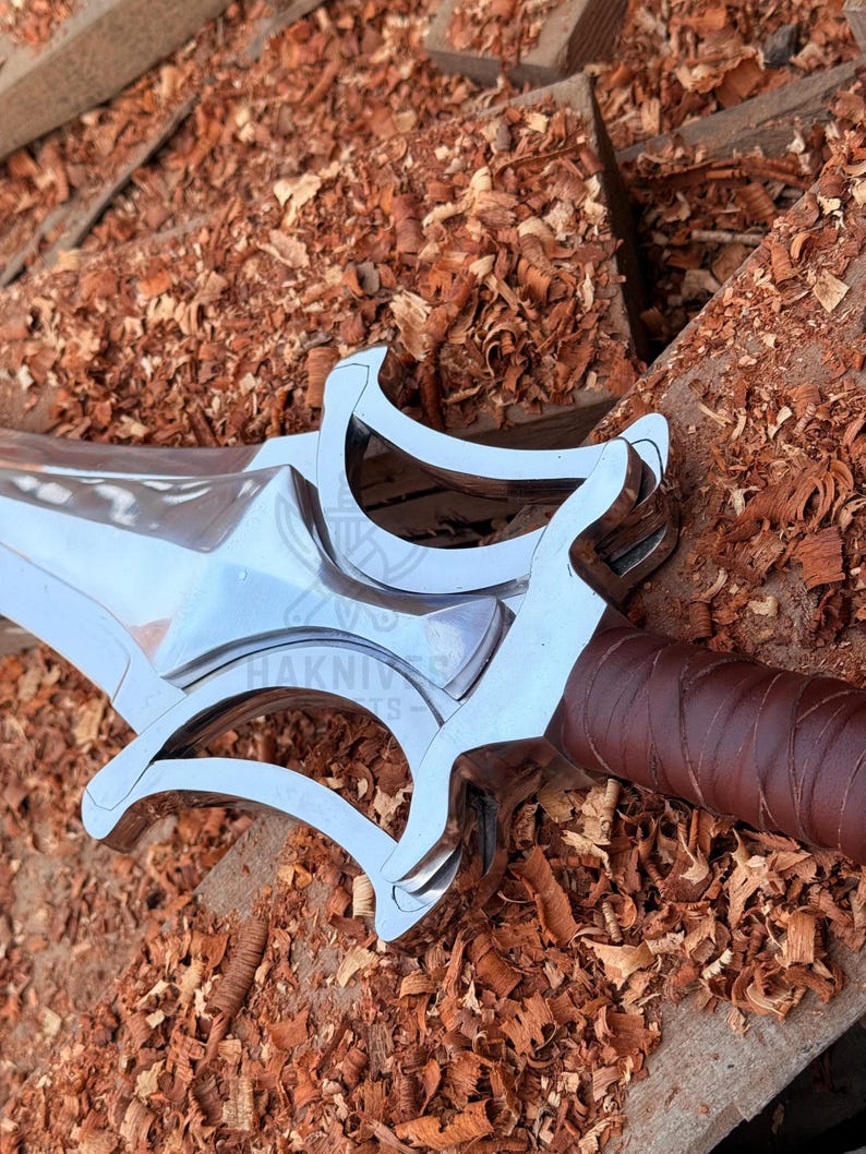 May include: A close-up of a silver sword with a brown leather-wrapped handle. The sword has a distinctive guard design and is set against a background of wood shavings.