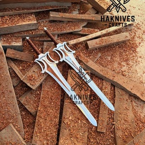 May include: Two decorative swords with silver blades and brown handles rest on a bed of wood shavings and planks. The swords have ornate, stylized hilts. The image includes the text "HAKNIVES CRAFTS" and a logo featuring a knife and axe.