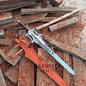 May include: A fantasy sword with a light blue blade and brown handle, resting on wooden planks. The sword has a decorative hilt and is accompanied by a brown leather sheath. The image includes the text "AKNIVE CRAFTS".