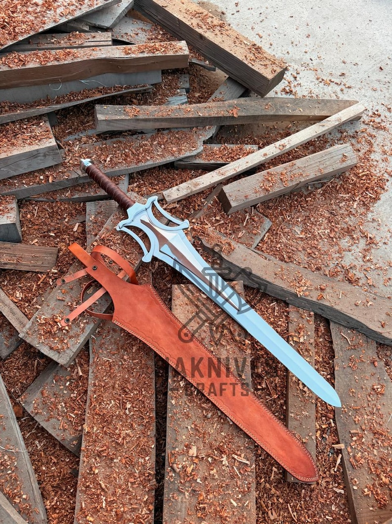 May include: A fantasy sword with a light blue blade and brown handle, resting on wooden planks. The sword has a decorative hilt and is accompanied by a brown leather sheath. The image includes the text "AKNIVE CRAFTS".