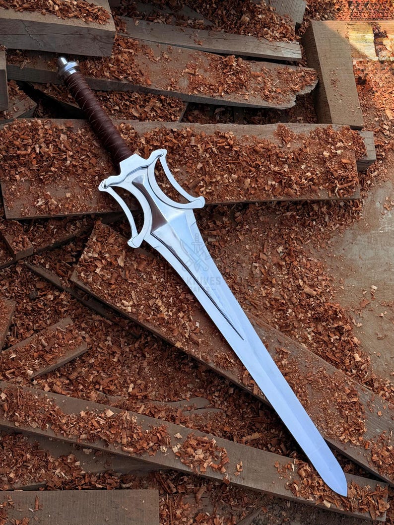 May include: A silver sword with a brown leather-wrapped handle. The blade is long and has a decorative hilt. The sword rests on wooden planks covered in wood shavings.
