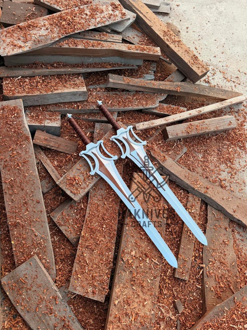 May include: Two decorative swords with silver blades and brown handles rest on a pile of wood. The swords have a distinctive design with a stylized hilt and a light blue blade. The text "KNIFE CRAFTS" is visible on the blade.