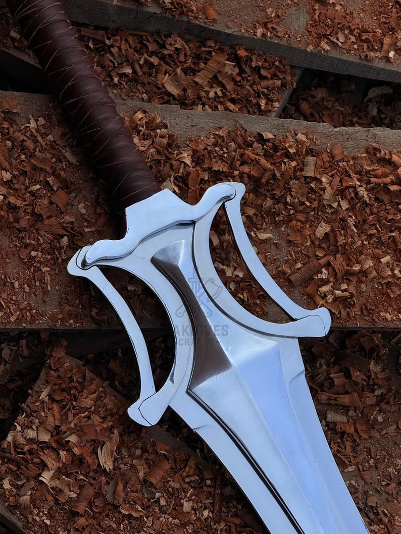 May include: A close-up of a silver sword with a brown leather-wrapped handle. The sword features a distinctive, stylized hilt with curved elements. The blade is polished and reflects light. The background is a wooden surface with wood shavings.