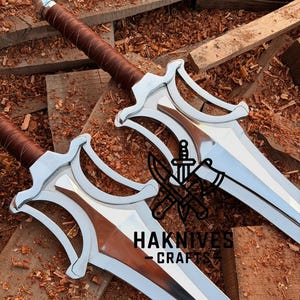 May include: Two silver swords with brown leather-wrapped handles and a copper-colored blade insert. The swords are displayed on a wooden surface with the text "HAKNIVES CRAFT".