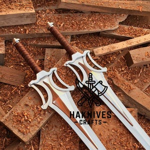 May include: Two silver and brown swords with intricate designs, featuring brown leather-wrapped handles and a polished blade. The swords are displayed on a wooden surface, with the text "HAKNIVES - CRAFTS" visible.