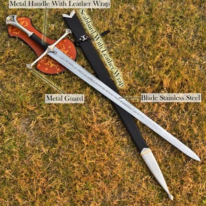 May include: A stainless steel sword with a metal guard and handle wrapped in leather. The sword is displayed with its black leather scabbard. The sword is resting on a brown surface.