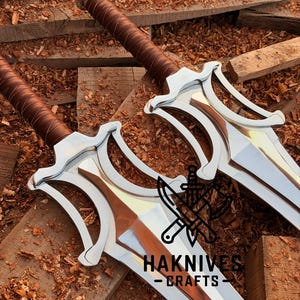 May include: Two swords with silver blades and brown leather-wrapped handles. The swords have a distinctive design with a curved guard. The image includes the text "HAKNIVES - CRAFTS".