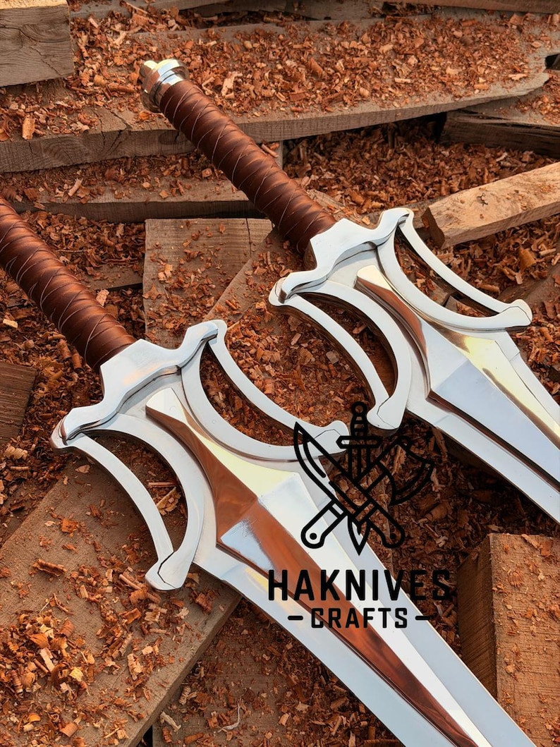 May include: Two swords with silver blades and brown leather-wrapped handles. The swords have a distinctive design with a curved guard. The image includes the text "HAKNIVES - CRAFTS".