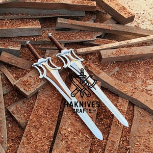 May include: Two silver and brown swords with ornate hilts rest on a pile of wooden planks and sawdust. The swords have a distinctive design with a curved guard and a brown leather-wrapped handle. The text "HAKNIVES CRAFTS" is visible.