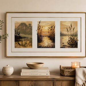 May include: A rectangular wall art piece featuring three separate cross-stitch landscape panels in a single gold frame. The artwork depicts a lake scene with a bird, a sunset over water with tall reeds, and a shoreline with aquatic plants in sepia tones.