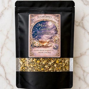 May include: A black pouch of "Moon Garden" tea by Sugar Siren Tea Co. The label features a moonlit scene with a teacup. The bottom of the pouch has a clear window showing the loose leaf tea. Net weight is 2 oz (56g).