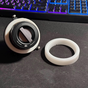 Könnte beinhalten: Ein schwarz-weißes DJI Focus Handwheel 2 mit einem weißen Ring auf einer dunklen Oberfläche. Das Handwheel hat ein Zifferblatt mit den Anzeigen "Tighten" und "Loosen". Im Hintergrund befindet sich eine Computertastatur.