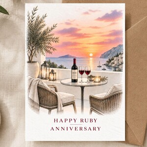 Op de afbeelding: Een wenskaart met een aquarelillustratie van een balkon met uitzicht op een zonsondergang boven zee, met twee stoelen, een tafel, een wijnfles en twee glazen. De tekst op de kaart luidt: HAPPY RUBY ANNIVERSARY in donkerrode hoofdletters.