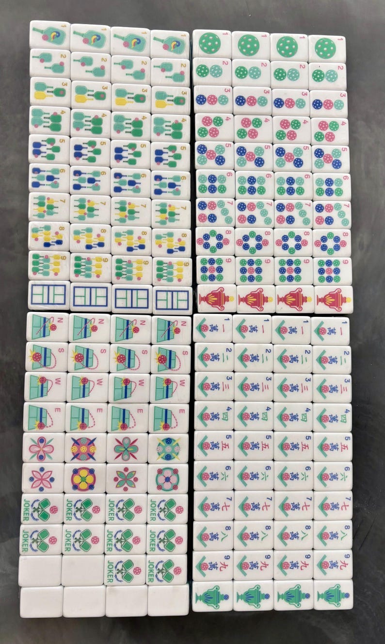 May include: A collection of white Mahjong tiles, each with unique symbols and numbers in various colors. The tiles feature designs like dots, flowers, and Chinese characters, arranged in a grid pattern.