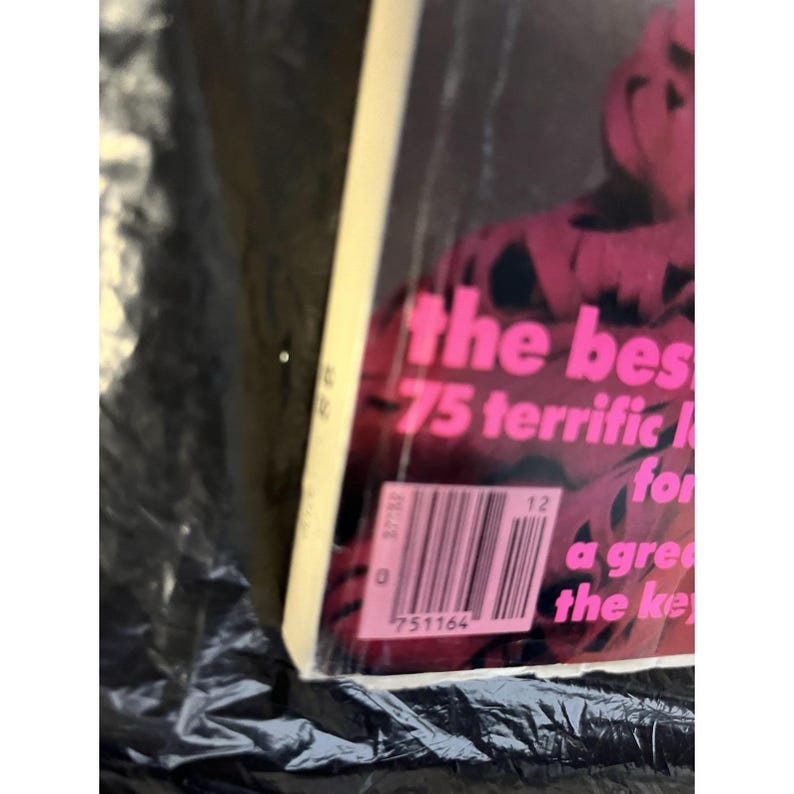 Puede incluir: Una portada de libro con el texto rosa "the bes 75 terrific" sobre un fondo oscuro. Un c&oacute;digo de barras y texto adicional son visibles en la esquina inferior derecha. El libro est&aacute; envuelto en pl&aacute;stico transparente.