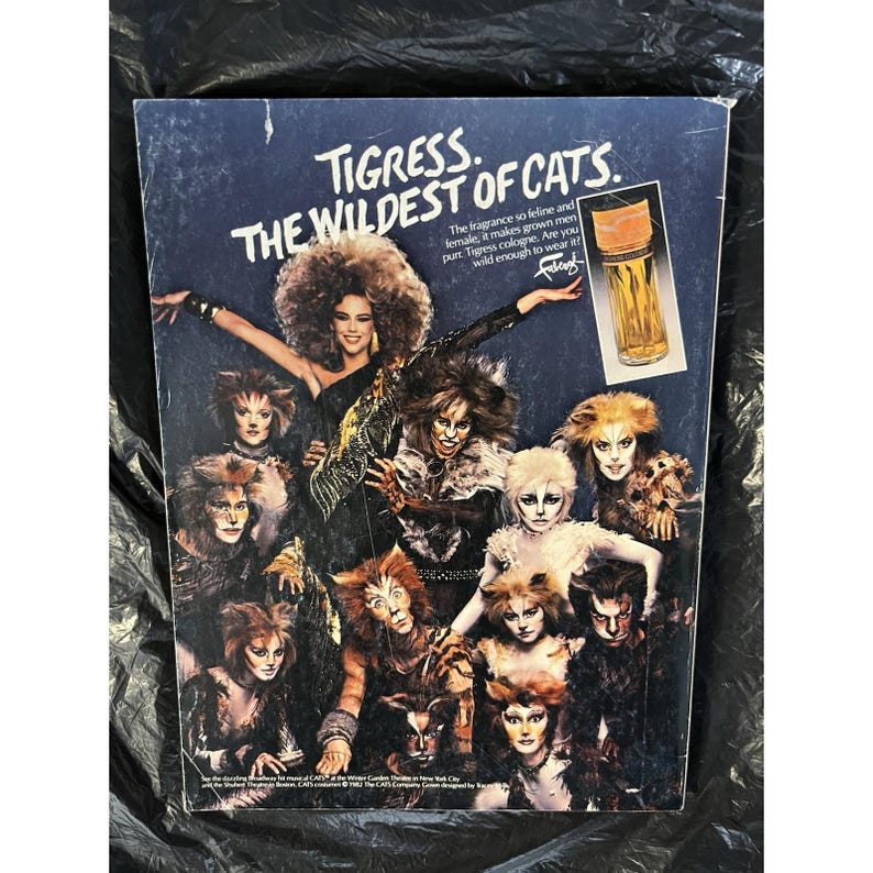Puede incluir: Un anuncio del perfume Tigress con un grupo de personas vestidas de gatos. El texto dice "Tigress. The Wildest of Cats". Se muestra un frasco de perfume. El fondo es azul oscuro.