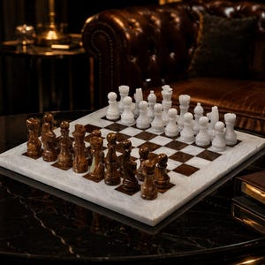 May include: A square chess set featuring a polished marble board with alternating white and dark brown squares. The set includes a full complement of carved stone chess pieces, with one side in solid white and the opposing side in a variegated brown.