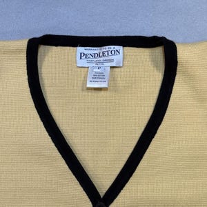 May include: A yellow cardigan with black trim and a V-neck. The cardigan has a single black button closure and a tag that reads "Pendleton, Portland, Oregon". The cardigan is made of a knit material.