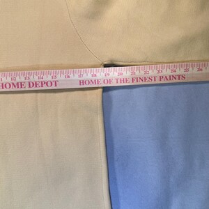May include: A cream-colored sweater with a black trim at the bottom and neckline. The sleeve is visible, and a ruler is placed across the garment. The text "HOME DEPOT" and "HOME OF THE FINEST PAINTS" are visible.