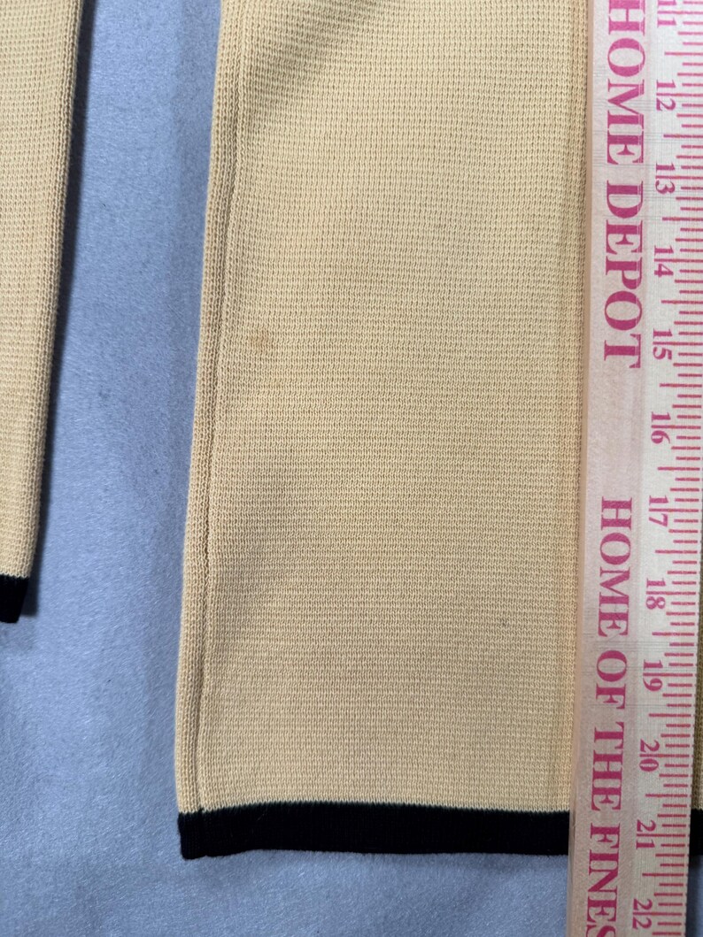 May include: Close-up of a beige knit garment with black trim at the bottom. A Home Depot ruler is placed next to the garment, showing measurements in inches. The text "HOME DEPOT" and "HOME OF THE FINES" are visible on the ruler.