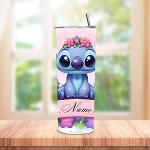 May include: A blue tumbler featuring a cartoon character with large eyes and a floral crown. The tumbler has a pink background with the character's image and the word "Name" on a banner. A straw is inserted in the lid.