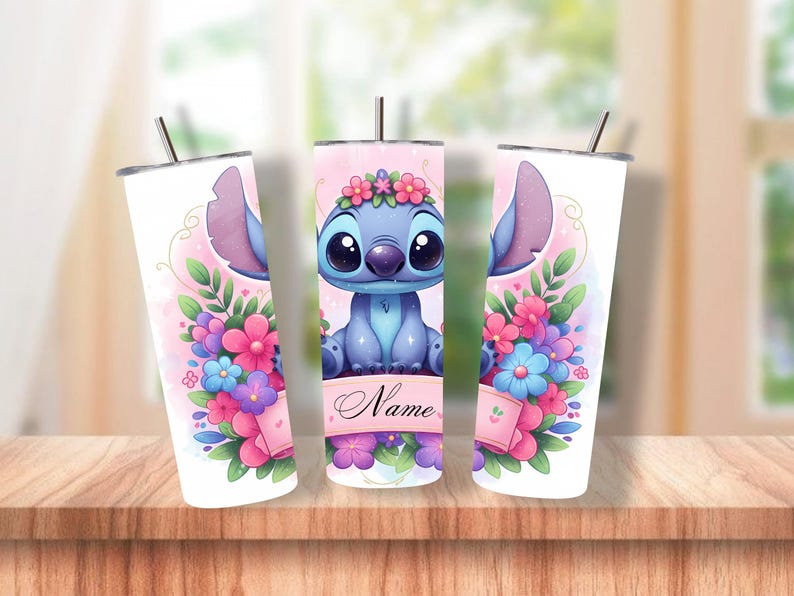 May include: A set of three white, insulated tumblers featuring a cartoon character with large ears and big eyes, surrounded by flowers. The character is blue with a flower crown. The tumblers have a pink and floral design with a straw.