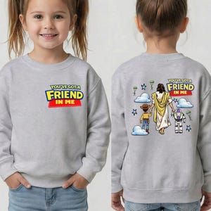 A young girl wearing a gray sweatshirt with a cartoon character and text on the back.