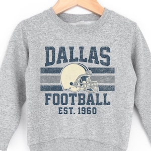 A grey sweatshirt with a graphic design featuring a football helmet and the text "DALLAS FOOTBALL EST. 1960".