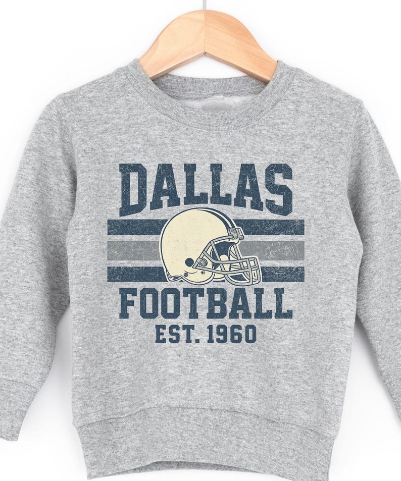 A grey sweatshirt with a graphic design featuring a football helmet and the text "DALLAS FOOTBALL EST. 1960".