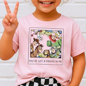 A young girl wearing a pink t-shirt with a graphic of characters from the Toy Story movie, including Woody, Buzz Lightyear, and other beloved characters, and the text "You've Got a Friend in Me".