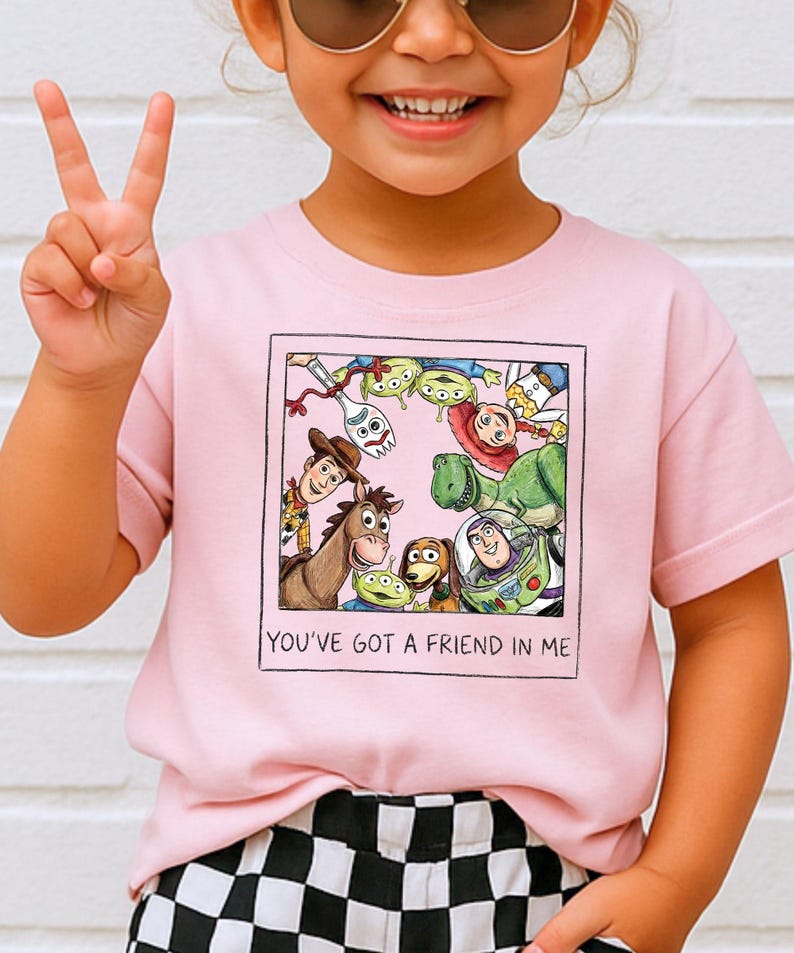 A young girl wearing a pink t-shirt with a graphic of characters from the Toy Story movie, including Woody, Buzz Lightyear, and other beloved characters, and the text "You've Got a Friend in Me".
