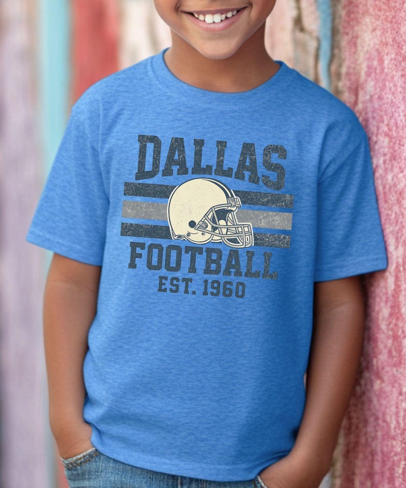 A young boy wearing a blue t-shirt with the text "DALLAS FOOTBALL EST. 1960" printed on it.