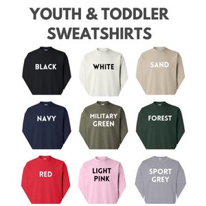a collection of youth and toddler sweatshirts in various colors, including black, white, sand, navy, military green, forest, red, pink, light pink, and grey.
