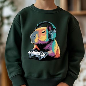 A child wearing a green sweatshirt with a colorful cartoon image of a capybara wearing headphones and holding a video game controller.