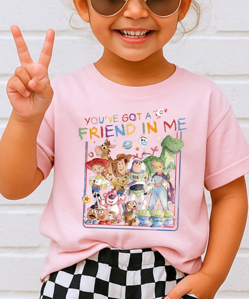 A young girl wearing a pink t-shirt with a colorful graphic of characters from the Toy Story movie, including Woody, Buzz Lightyear, and other beloved characters.