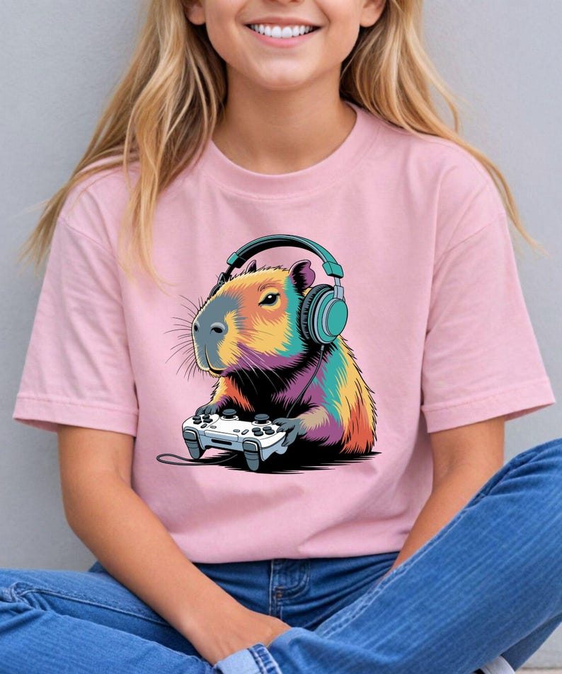 A woman wearing a pink t-shirt with a colorful cartoon image of a capybara wearing headphones and holding a video game controller.
