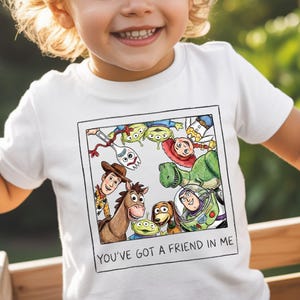 A young child wearing a white t-shirt with a collage of characters from the Toy Story movie, including Woody, Buzz Lightyear, and other beloved characters.