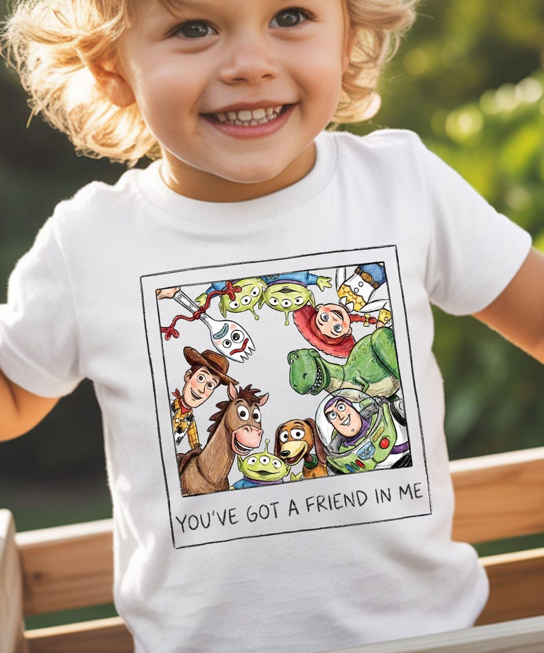 A young child wearing a white t-shirt with a collage of characters from the Toy Story movie, including Woody, Buzz Lightyear, and other beloved characters.