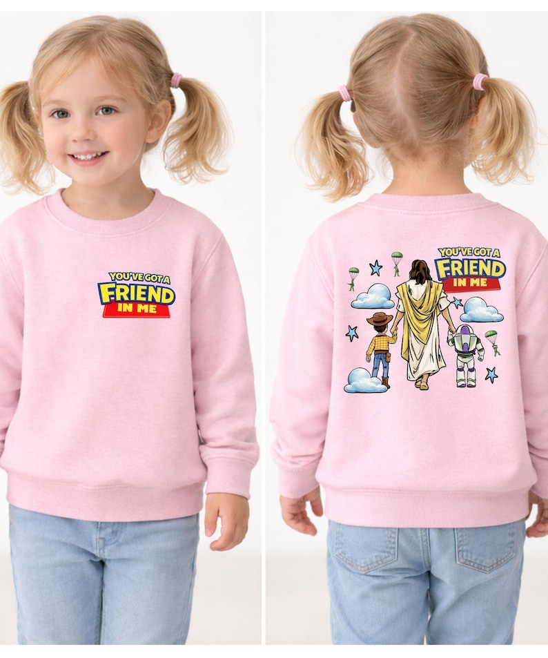 A young girl wearing a pink sweater with a cartoon image of Jesus Christ and the words "You're a friend in me" printed on it.