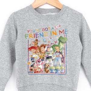 A gray sweatshirt with a colorful graphic design featuring characters from the Toy Story movie, including Woody, Buzz Lightyear, and other beloved characters.
