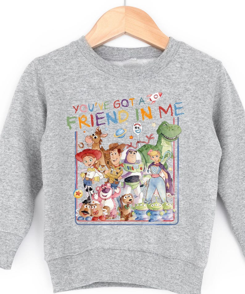 A gray sweatshirt with a colorful graphic design featuring characters from the Toy Story movie, including Woody, Buzz Lightyear, and other beloved characters.