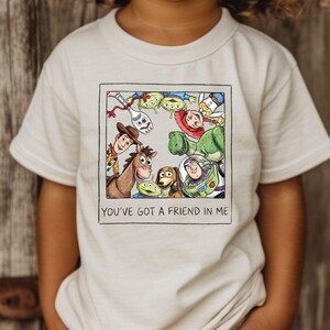 A child wearing a white t-shirt with a graphic of characters from the Toy Story movie, including Woody, Buzz Lightyear, and other beloved characters.