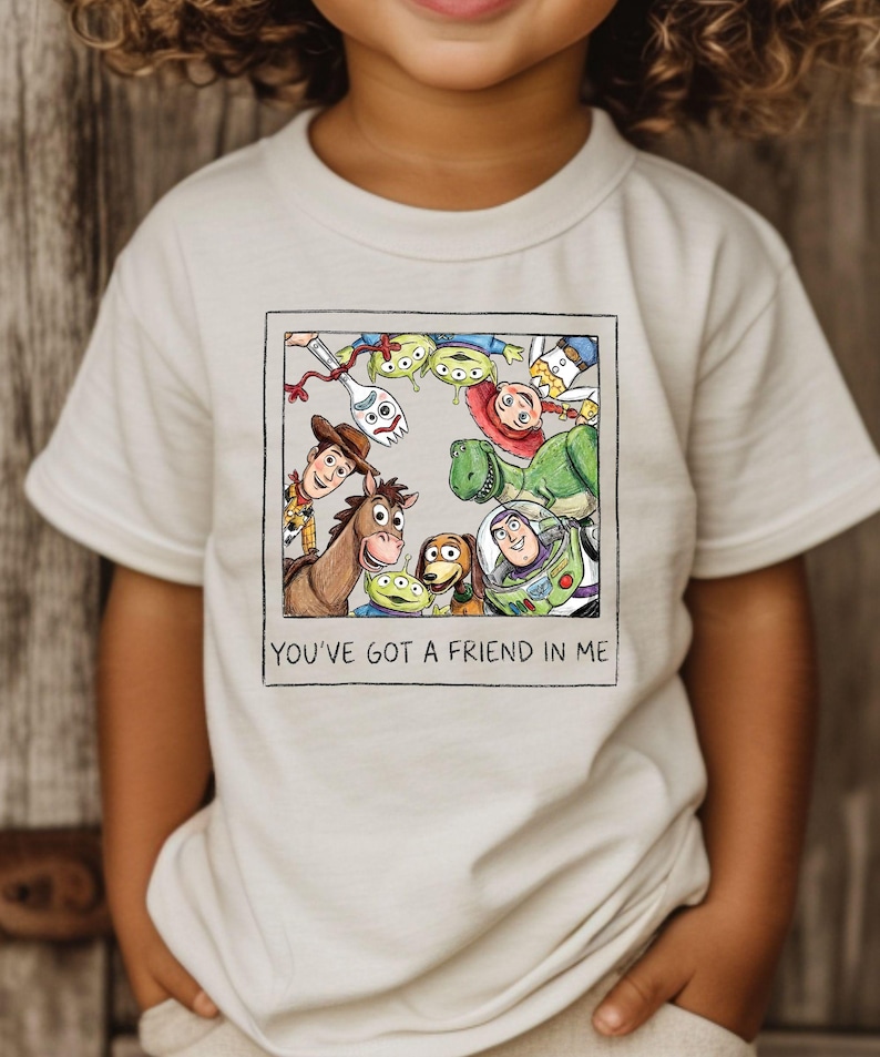 A child wearing a white t-shirt with a graphic of characters from the Toy Story movie, including Woody, Buzz Lightyear, and other beloved characters.