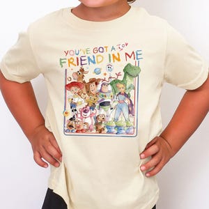 A young girl wearing a white t-shirt with a colorful graphic of characters from the Toy Story movie, including Woody, Buzz Lightyear, and other beloved characters.