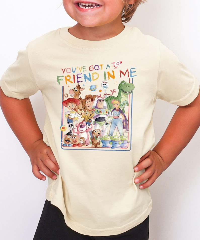 A young girl wearing a white t-shirt with a colorful graphic of characters from the Toy Story movie, including Woody, Buzz Lightyear, and other beloved characters.