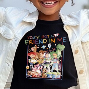 A young girl wearing a black t-shirt with a colorful graphic of characters from the Toy Story movie, including Woody, Buzz Lightyear, and other beloved characters.