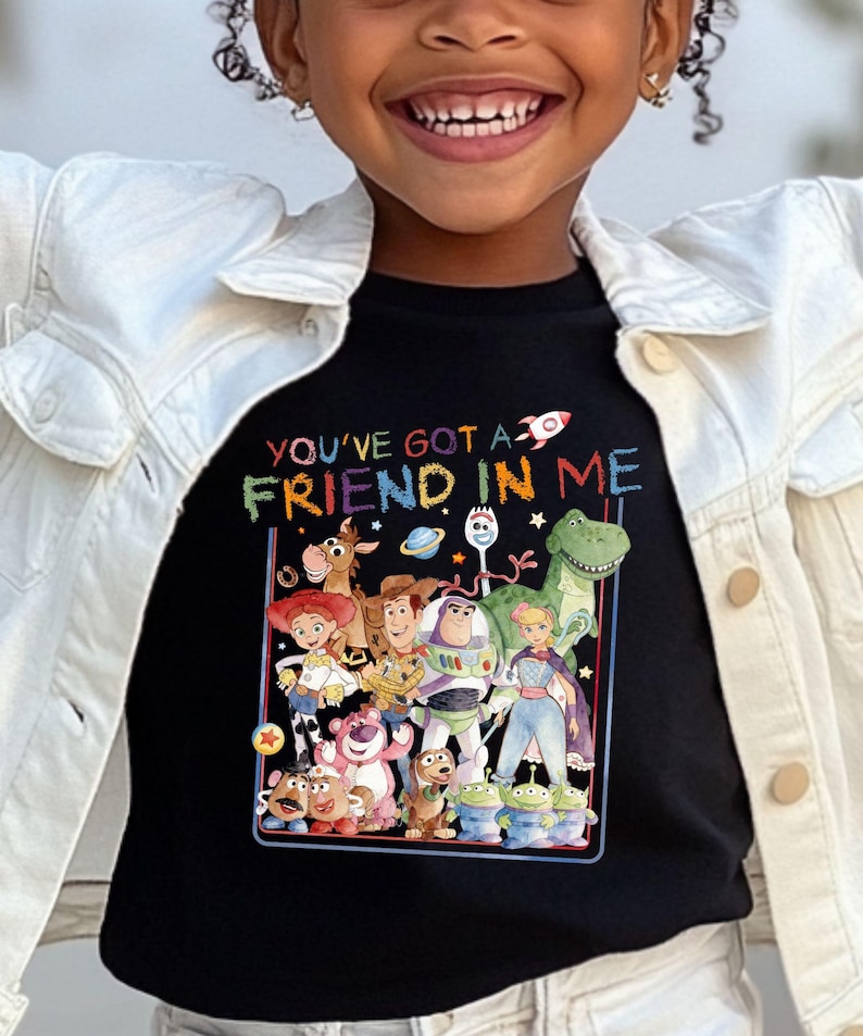 A young girl wearing a black t-shirt with a colorful graphic of characters from the Toy Story movie, including Woody, Buzz Lightyear, and other beloved characters.