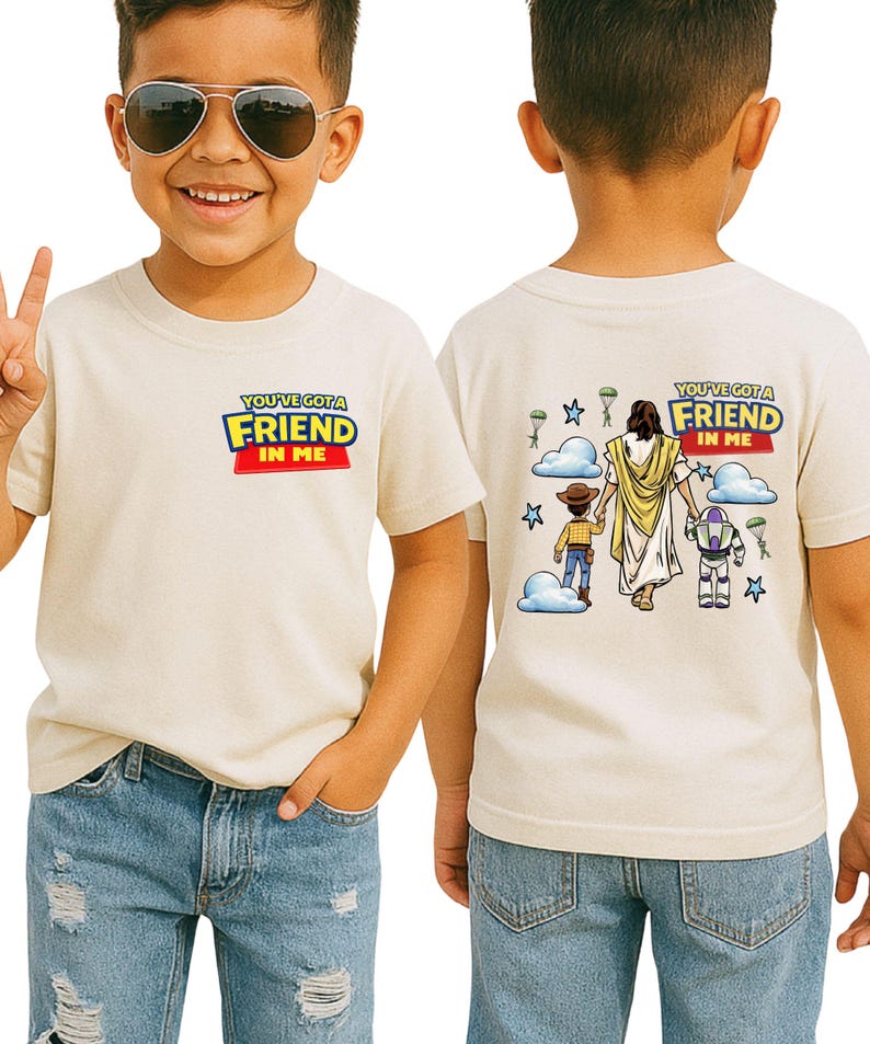 A young boy wearing a white t-shirt with a graphic design and text on the back, smiling and making a peace sign.